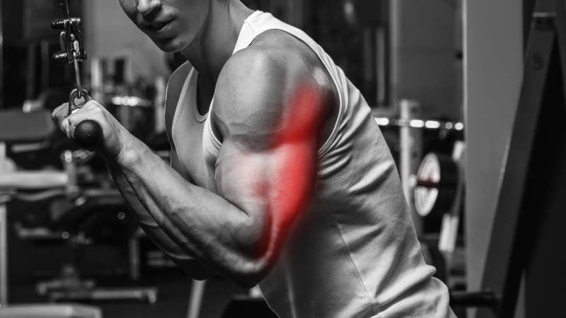 Moški trenira triceps v fitnesu, pri čemer je mišica poudarjena z rdečo barvo, kar ponazarja zavestno povezavo med možgani in mišico.
