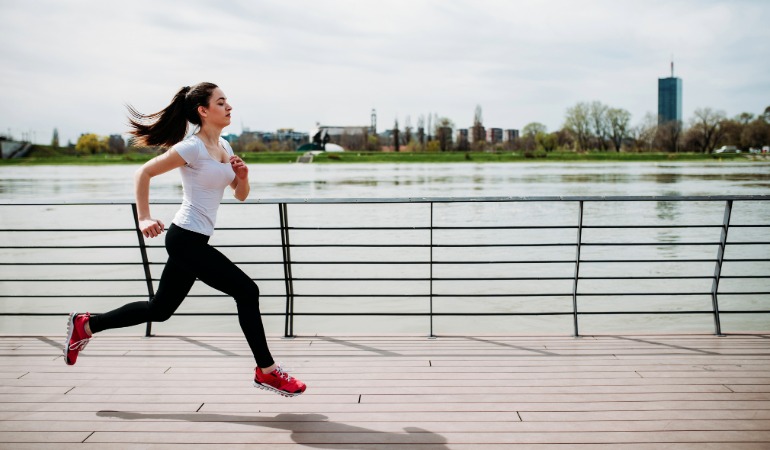 Tekačica med fartlek treningom ob reki v urbanem okolju, kar ponazarja fleksibilnost izvajanja "igre hitrosti".